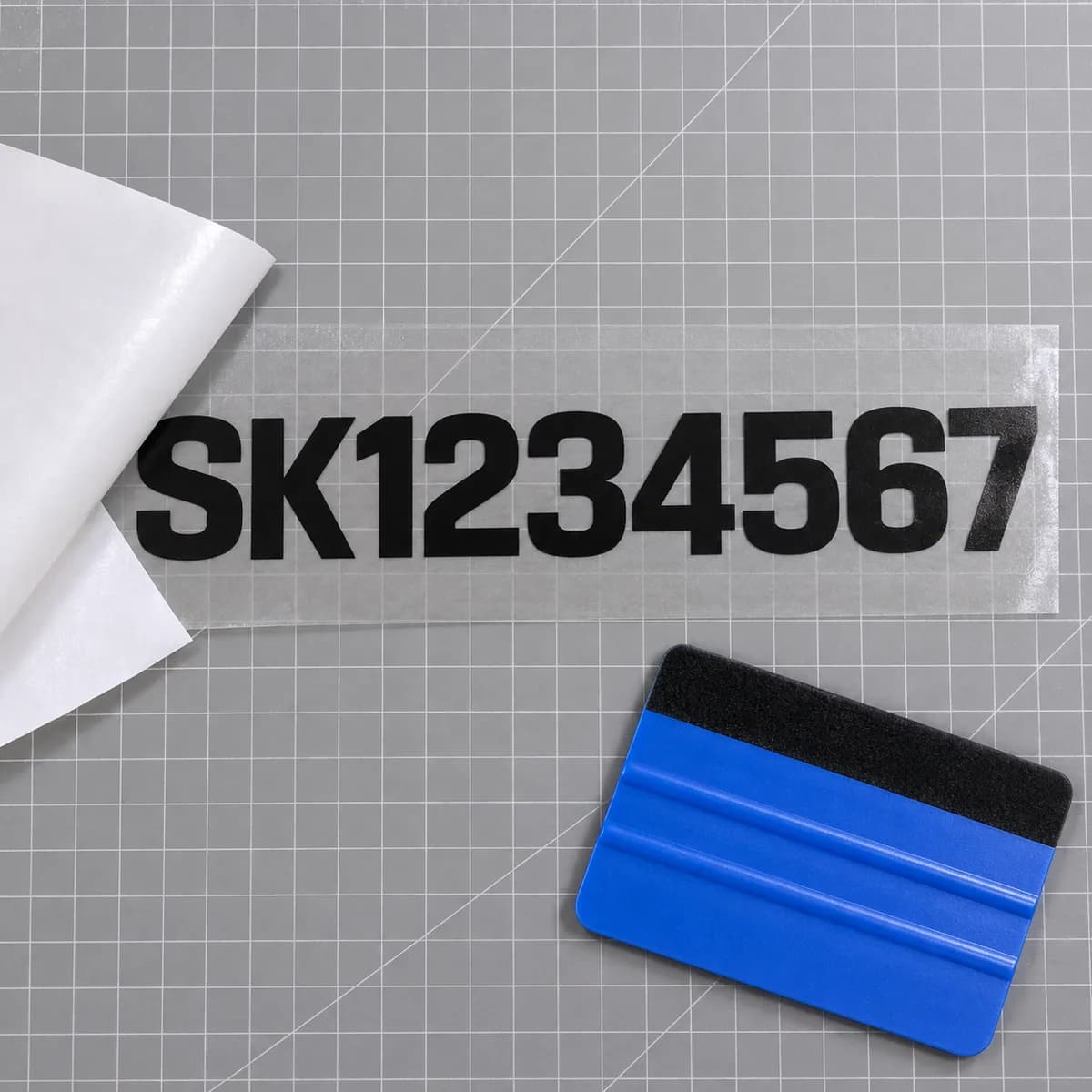 Die-cut black vinyl SK boat registration number lettering on clear premask transfer tape with a squeegee, ready to apply